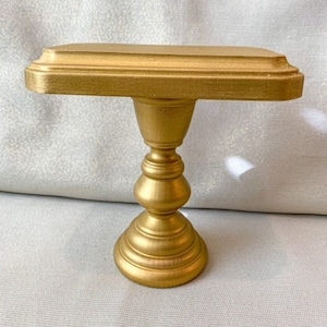 May include: A gold-colored cake stand with a round top and a pedestal base. The stand is made of wood and has a smooth, polished finish.