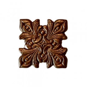 May include: A decorative metal ornament with a square shape and a detailed floral design. The ornament is made of a metallic bronze color.
