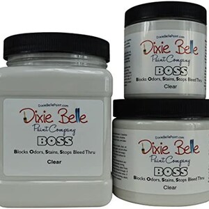May include: Three bottles of Dixie Belle Paint Company BOSS clear paint. The bottles are labeled with the company name, product name, and a description of the product's features. The bottles are different sizes.
