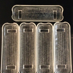 May include: A collection of five clear glass rectangular light lenses. Four are vertically oriented, and one is horizontal. Each has a textured surface and a rectangular inset. The lenses are likely for a vehicle.