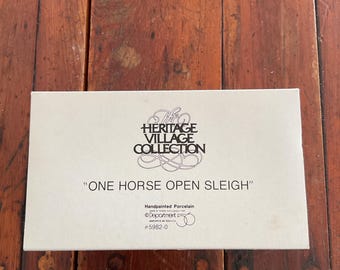 May include: A rectangular box with the text "The Heritage Village Collection" and "One Horse Open Sleigh". The box is hand-painted porcelain and has the Department 56 logo and product number.