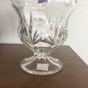 May include: Clear crystal Marquis by Waterford vase with a scalloped rim and a pedestal base. The vase features a cut glass design and a sticker that reads "MARQUIS by Waterford".