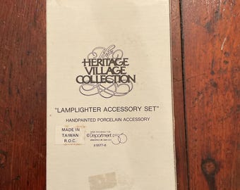 May include: A rectangular box with the text "The Heritage Village Collection" and "Lamplighter Accessory Set." The box is white with black text and features a hand-painted porcelain accessory. Made in Taiwan.