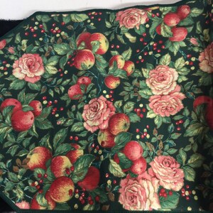 K&ouml;nnte beinhalten: Ein rechteckiger Stoff mit dunkelgr&uuml;nem Hintergrund, der ein Muster aus roten &Auml;pfeln, rosa Rosen und kleinen roten Beeren aufweist. Die Kanten sind mit einem dunkelgr&uuml;nen Rand versehen.