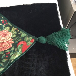 K&ouml;nnte beinhalten: Dekorativer Tischl&auml;ufer mit einem Blumenmuster aus rosa Rosen und roten &Auml;pfeln auf dunkelgr&uuml;nem Grund. Er hat eine gr&uuml;ne Quaste und liegt auf einer schwarzen, strukturierten Oberfl&auml;che. Dekorationsartikel.