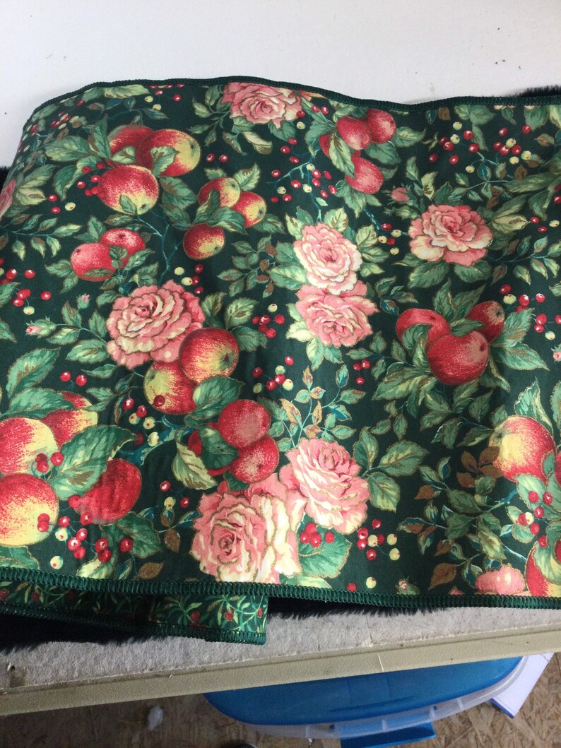 K&ouml;nnte beinhalten: Dunkelgr&uuml;ner Stoff mit einem Muster aus roten &Auml;pfeln, rosa Rosen und roten Beeren. Der Stoff hat einen gr&uuml;nen Rand mit einem kleinen Blumenmuster. Das Design ist ein Vintage-Botanisches Muster, geeignet f&uuml;r verschiedene Bastelprojekte.