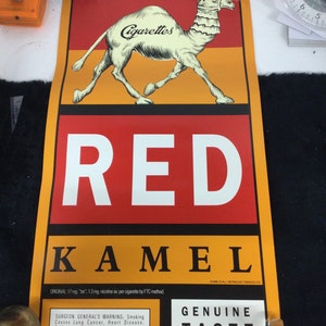 May include: A vintage Red Kamel cigarettes advertisement. The poster features a camel illustration above the words "Cigarettes" and "RED KAMEL" in bold white letters. The poster includes the Surgeon General's warning and the words "GENUINE TASTE".