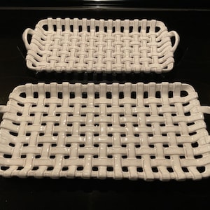 May include: Two white ceramic serving trays with a woven basket design. The trays are rectangular with rounded handles on each end. The larger tray is approximately 16 inches long, and the smaller tray is about 12 inches long.