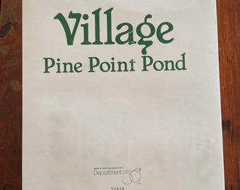 May include: A cream-colored paper product with the words "Village Pine Point Pond" in green lettering. The product also features the text "Made in China Exclusively for Department 56" and the number "52618".