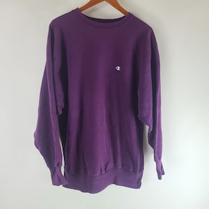 May include: A purple Champion sweatshirt with a small white logo on the left chest.