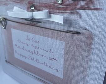 May include: A handmade birthday card with a white background and a pink and white floral design. The card features a white ribbon, clear rhinestones, and the handwritten message "To Our Very Special Daughter Happy 21st Birthday."
