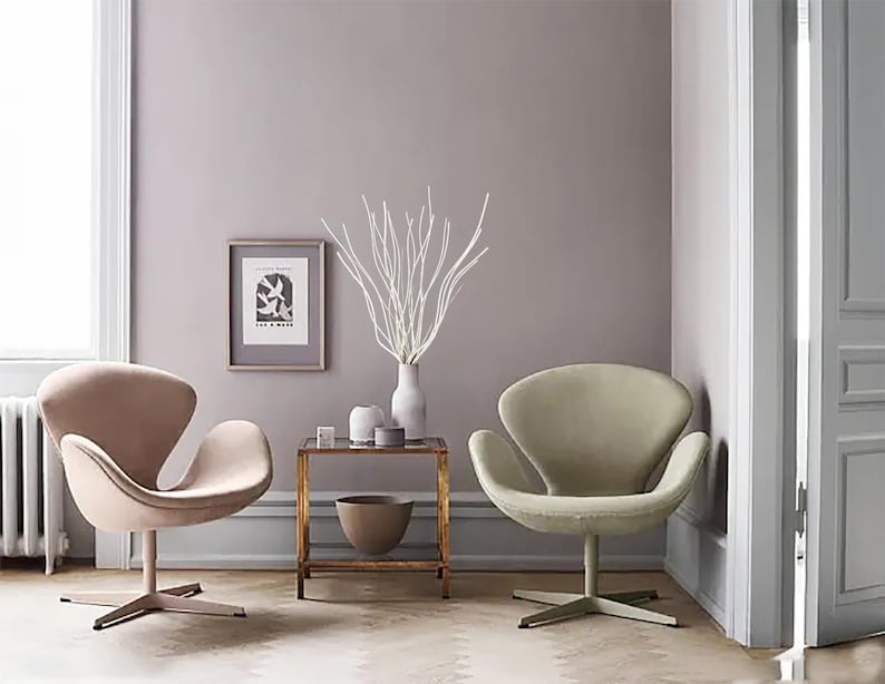 May include: Two white swan chairs in a living room setting with a side table and a vase with white branches. The walls are painted a light purple color.