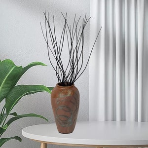 May include: A brown ceramic vase with a swirling pattern, filled with black twig branches. The vase is sitting on a white table.