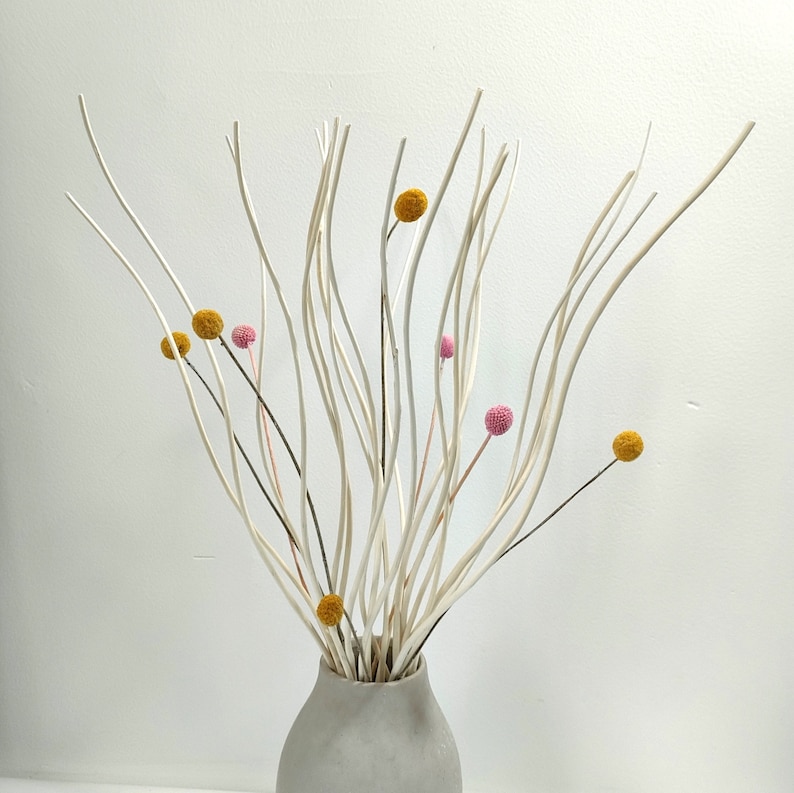 May include: A white ceramic vase with a bouquet of dried white branches and yellow and pink flower heads.