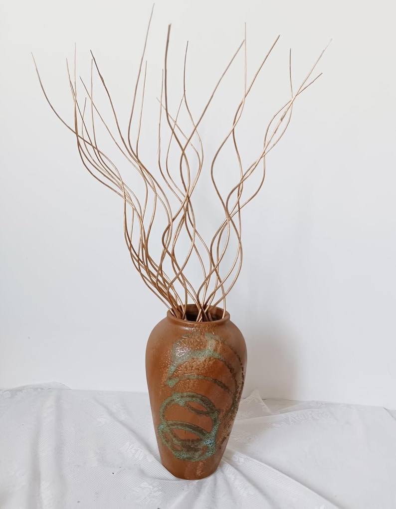 May include: A brown ceramic vase with a textured surface and green accents. The vase is filled with thin, brown, curly branches.
