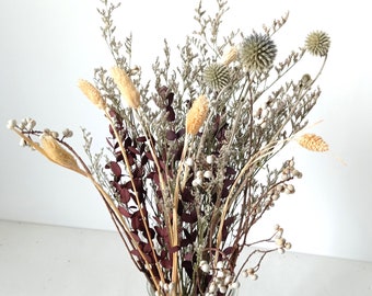 May include: A dried flower arrangement in a clear glass vase. The bouquet features a variety of dried flowers and grasses in shades of brown, beige, and white.