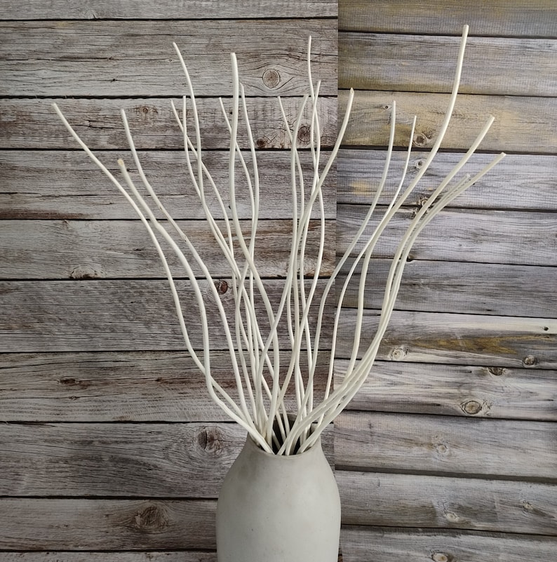 May include: A white ceramic vase filled with white, slender branches. The vase is on a wooden background.