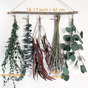 May include: A wall hanging featuring five varieties of dried plants and flowers. The hanging is made from a natural branch measuring 16-17 inches or 42 cm in length. The plants include boxwood leaves, eucalyptus, dried lavender, and two types of dried leaves.