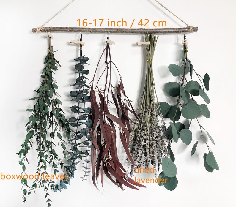 May include: A wall hanging featuring five varieties of dried plants and flowers. The hanging is made from a natural branch measuring 16-17 inches or 42 cm in length. The plants include boxwood leaves, eucalyptus, dried lavender, and two types of dried leaves.