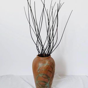May include: A brown ceramic vase with a textured surface and green and brown swirling designs. The vase is filled with black twig-like branches.