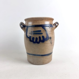 Pode incluir: Um pote de grés castanho com duas pegas pequenas e um desenho azul semelhante a uma mão. O recipiente cilíndrico tem uma faixa azul na parte superior e inferior. O pote de estilo antigo é adequado para a cozinha ou decoração de casa.