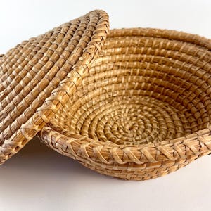 Puede incluir: Una cesta de mimbre tejida con tapa. La cesta est&aacute; hecha de paja natural y tiene forma redonda. La tapa encaja perfectamente en la parte superior de la cesta.