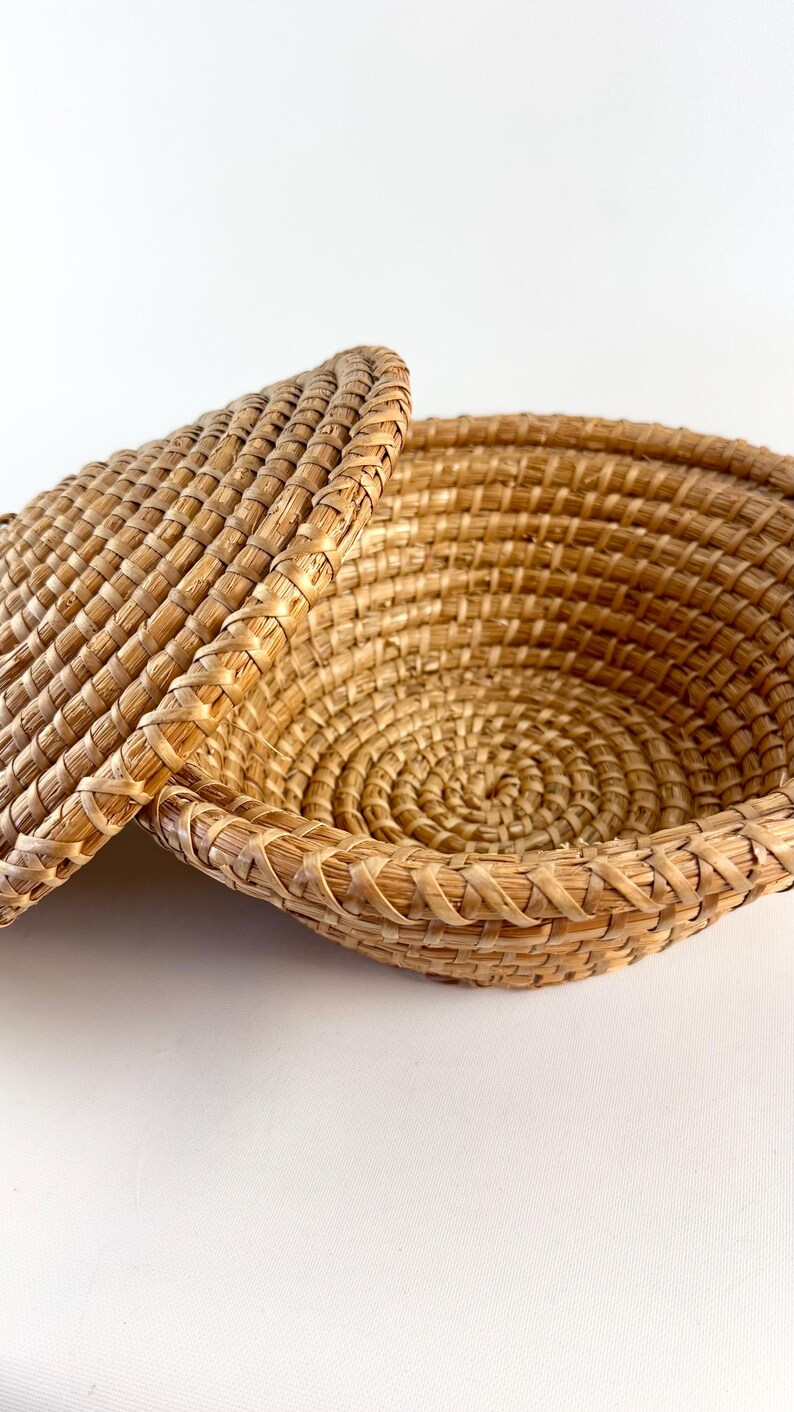Puede incluir: Una cesta de mimbre tejida con tapa. La cesta est&aacute; hecha de paja natural y tiene forma redonda. La tapa encaja perfectamente en la parte superior de la cesta.
