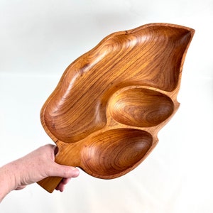 Op de afbeelding: Een houten serveerschaal in de vorm van een blad met drie ovale compartimenten. De schaal is gemaakt van lichtbruin hout met zichtbare nerfpatronen. Het heeft een handvat aan één uiteinde.
