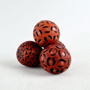 May include: Four orange decorative spheres with black abstract patterns. The spheres are arranged in a small pile, with three visible and one partially obscured. The background is a plain white surface.