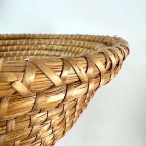 Puede incluir: Primer plano del borde tejido de una cesta de mimbre grande, redonda y de color natural.