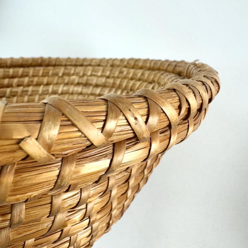 Puede incluir: Primer plano del borde tejido de una cesta de mimbre grande, redonda y de color natural.