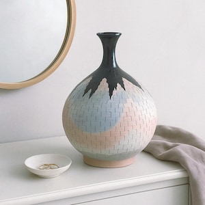 May include: A large, round ceramic vase with a black neck and a textured, abstract design in shades of pink, blue, and white.