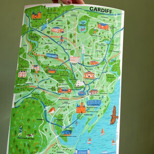 May include: A colorful illustrated map of Cardiff, Wales, with green parks, blue water, and red buildings. The map includes landmarks like Cardiff Castle, Cardiff Bay, and the Millennium Centre. The text "CARDIFF" is printed in large, bold letters at the top of the map.
