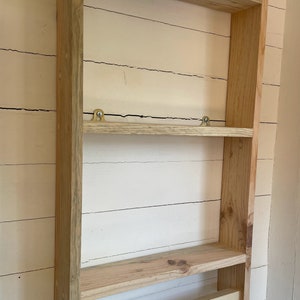 May include: A wooden wall shelf with two shelves and a towel bar. The shelf is made of unfinished pine wood and has a simple, rustic design.
