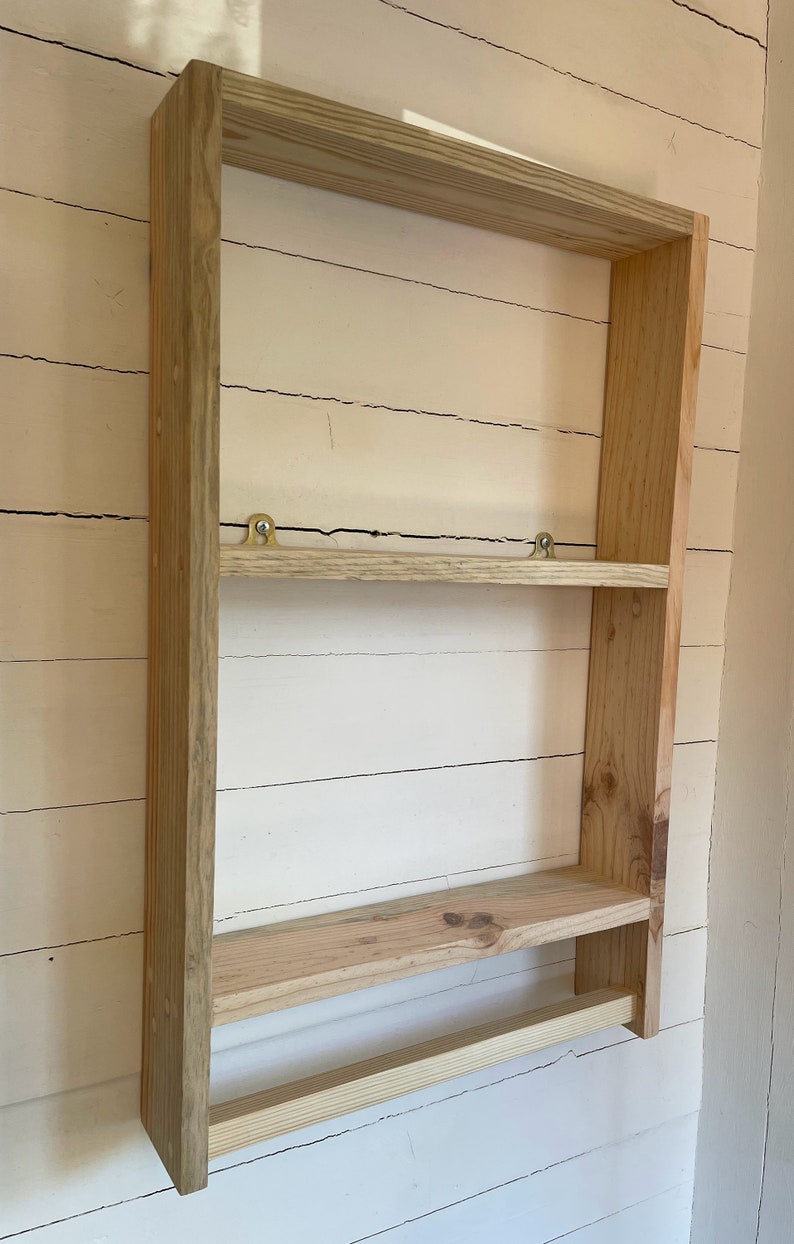 May include: A wooden wall shelf with two shelves and a towel bar. The shelf is made of unfinished pine wood and has a simple, rustic design.