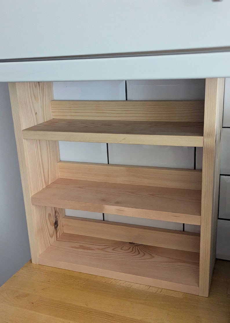 May include: A natural wood shelf unit with three shelves. The shelves are made of unfinished wood and have a light brown colour.