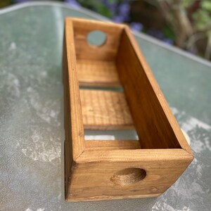 May include: A small wooden box with two holes on the sides. The box is made of natural wood and has a rustic look.