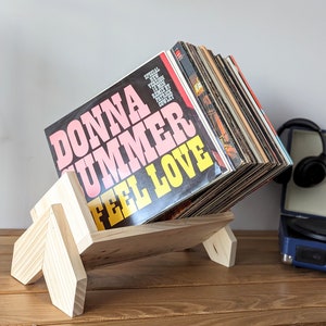May include: A wooden record stand with a stack of vinyl records. The top record is a pink and yellow album with the title "Donna Summer Feel Love".