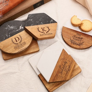 May include: A selection of personalised coasters with a wood and marble design. The coasters feature engraved names and dates, in various shapes such as round, square, and hexagonal. Some coasters have the text "Deborah EST. 2021", "Kathleen", and "The Scarlett Family".