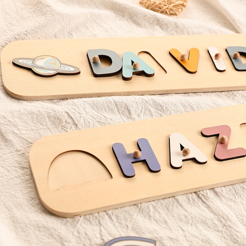 Może przedstawiać: Dwa drewniane puzzle z nazwami z kolorowymi literami. G&oacute;rny puzzle ma nazwę "DAVID" z niebieską planetą i pierścieniami. Dolny puzzle ma nazwę "HAZ" z p&oacute;łkolistym wycięciem.