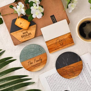 May include: A selection of personalised coasters. One is hexagonal with a black and wood grain finish, another is square with a white and wood grain finish, and two are round with a wood grain and stone finish. Each coaster features custom text and designs.
