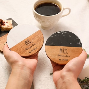 以下が含まれることがあります： 黒と白の大理石模様の丸いコースター2枚。1枚は「MR. Alexander EST 2022」と書いてあり、もう1枚は「MRS. Alexander EST 2022」と書いてあります。