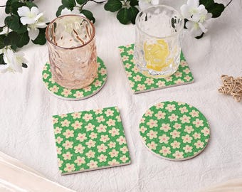 May include: Four ceramic drink coasters with a floral pattern. Two are square and two are round. The coasters have a green background with a repeating pattern of small, light pink flowers. Two glasses are on top of the coasters.