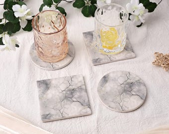 May include: Two clear textured drinking glasses and four coasters with a white and gray marble pattern. One glass is tinted light pink, and the other is clear with a yellow base. Two coasters are circular, and two are square in shape.