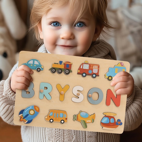 Transportation-themed wooden name puzzle with 419 favorites — each letter is a different vehicle (train, plane, car), making it a personalized Montessori toy that kids actually play with and parents adore gifting.