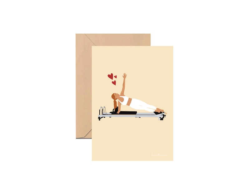 May include: A greeting card featuring a cartoon illustration of a person performing a pilates exercise on a reformer machine. The person is wearing white clothing and there are red hearts floating above them.