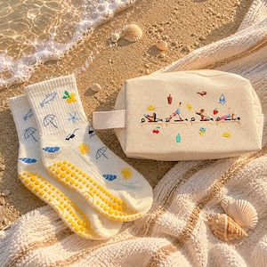 May include: A pair of cream-colored socks with blue umbrellas, clouds, and lemons, and a beige cosmetic bag with embroidered figures doing yoga. The socks have yellow non-slip grips on the soles. The bag has a small handle.