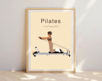 May include: A framed Pilates art print. The image shows a woman using a Pilates reformer machine. The text "Pilates is my happy place" is in brown on a cream background. The frame is a light wood colour.