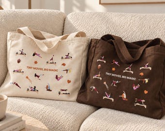 Puede incluir: Dos bolsas de tela, una color crema y otra marrón oscuro, cada una con un patrón repetitivo de pequeñas figuras realizando ejercicios de Pilates en máquinas, junto con el texto "TINY MOVES, BIG MAGIC" impreso en el centro de cada bolsa.
