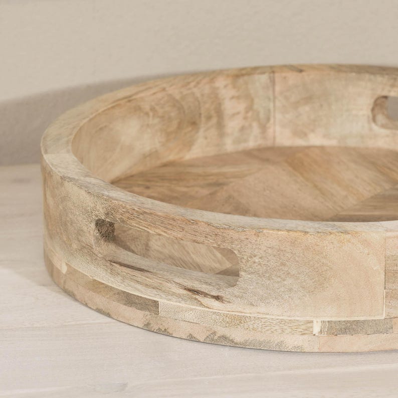 May include: A round wooden tray with a light brown finish. The tray has a unique design with a raised edge and cut-out handles on the sides.